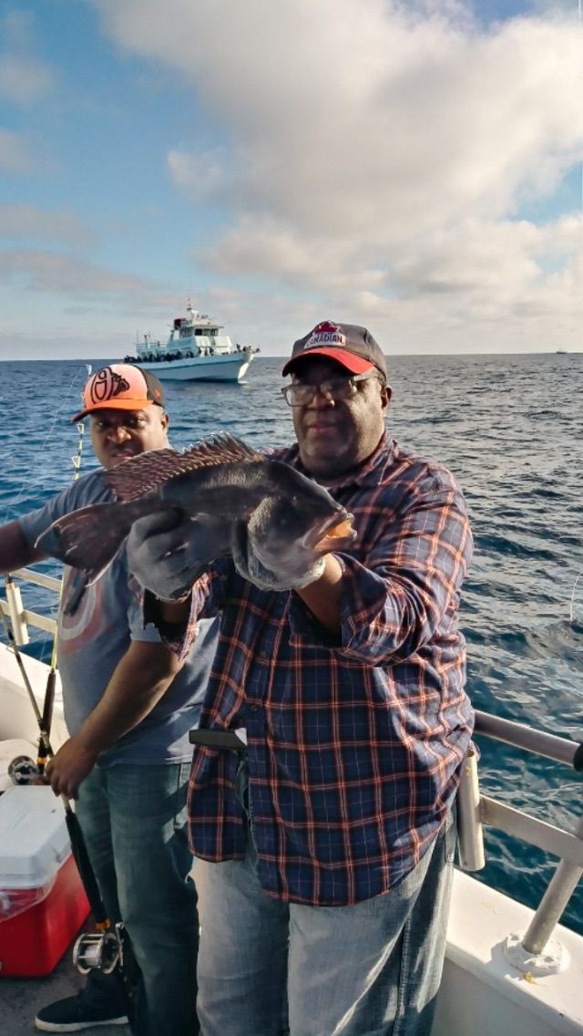 Two men are standing on a boat holding a large fish.