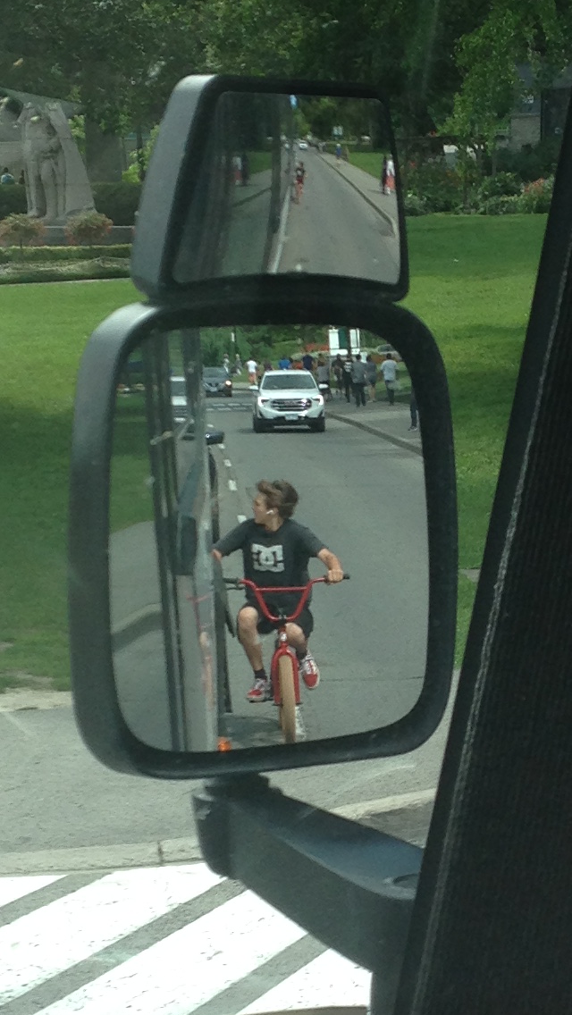 A boy is riding a bike in the rear view mirror of a car.