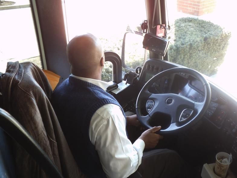A man is driving a bus and looking out the window
