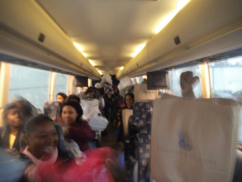 A group of people sitting on a bus with a bag that says prada on it