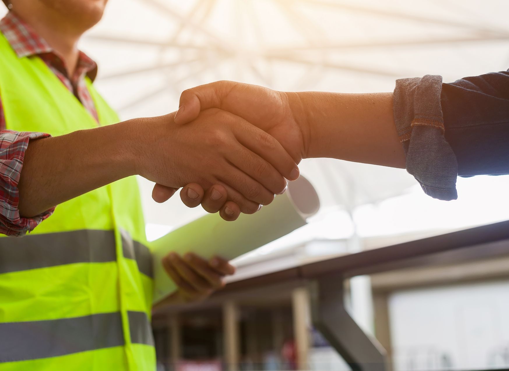 A construction worker is shaking hands with a client while holding a blueprint.