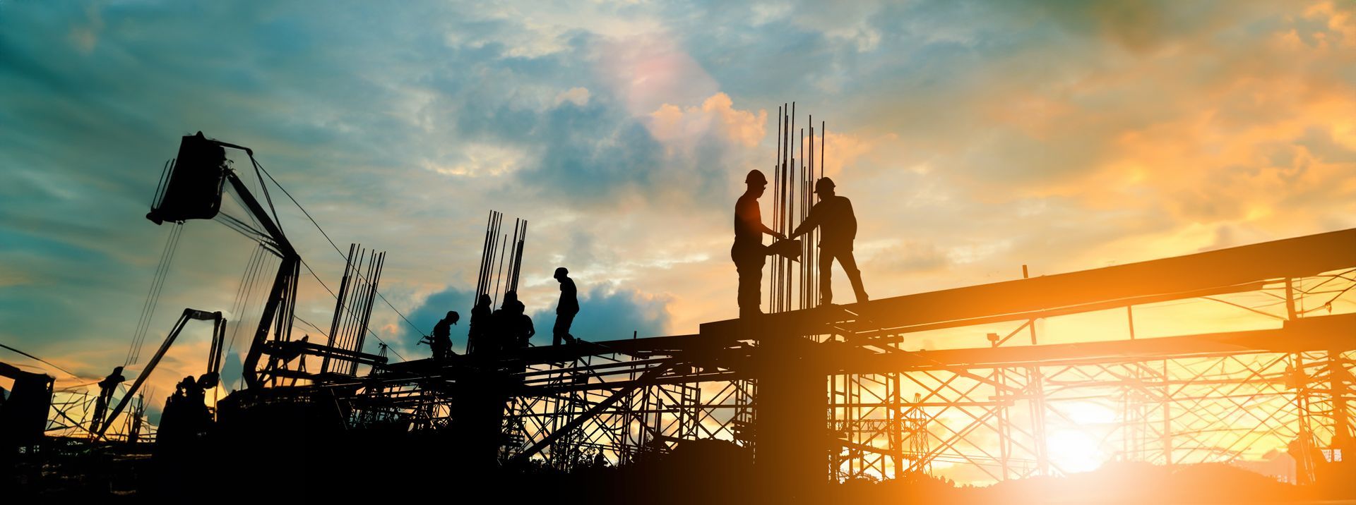 A group of construction workers are working on a building at sunset.