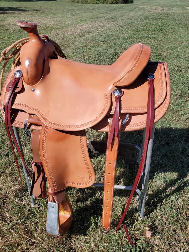 Tan western saddle with brown leather and black straps displayed on grass outdoors