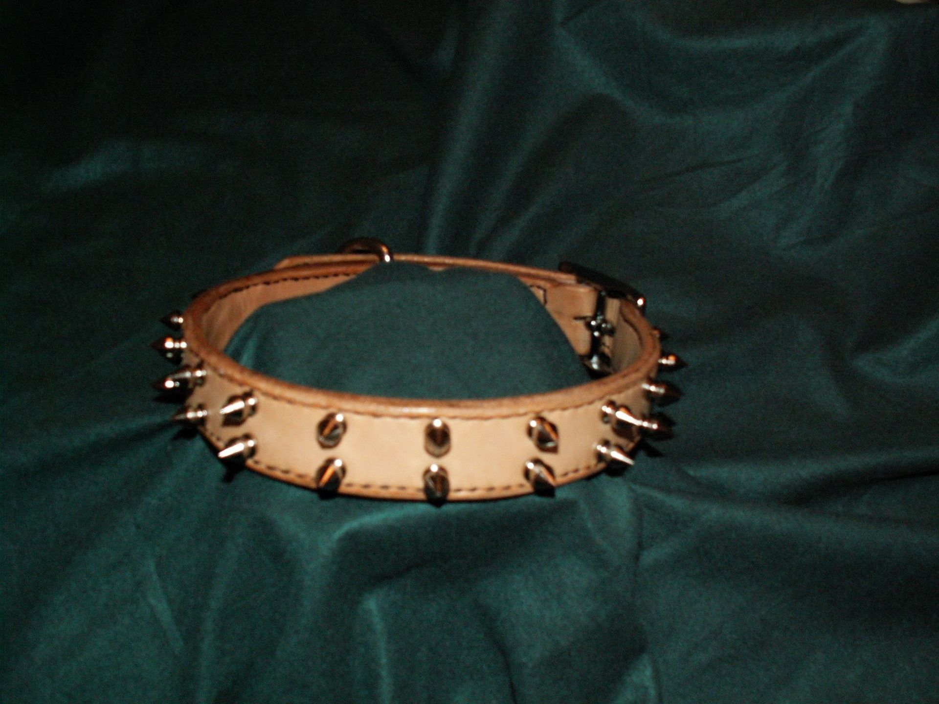 Tan leather studded wrist cuff with metal spikes on a dark green fabric background