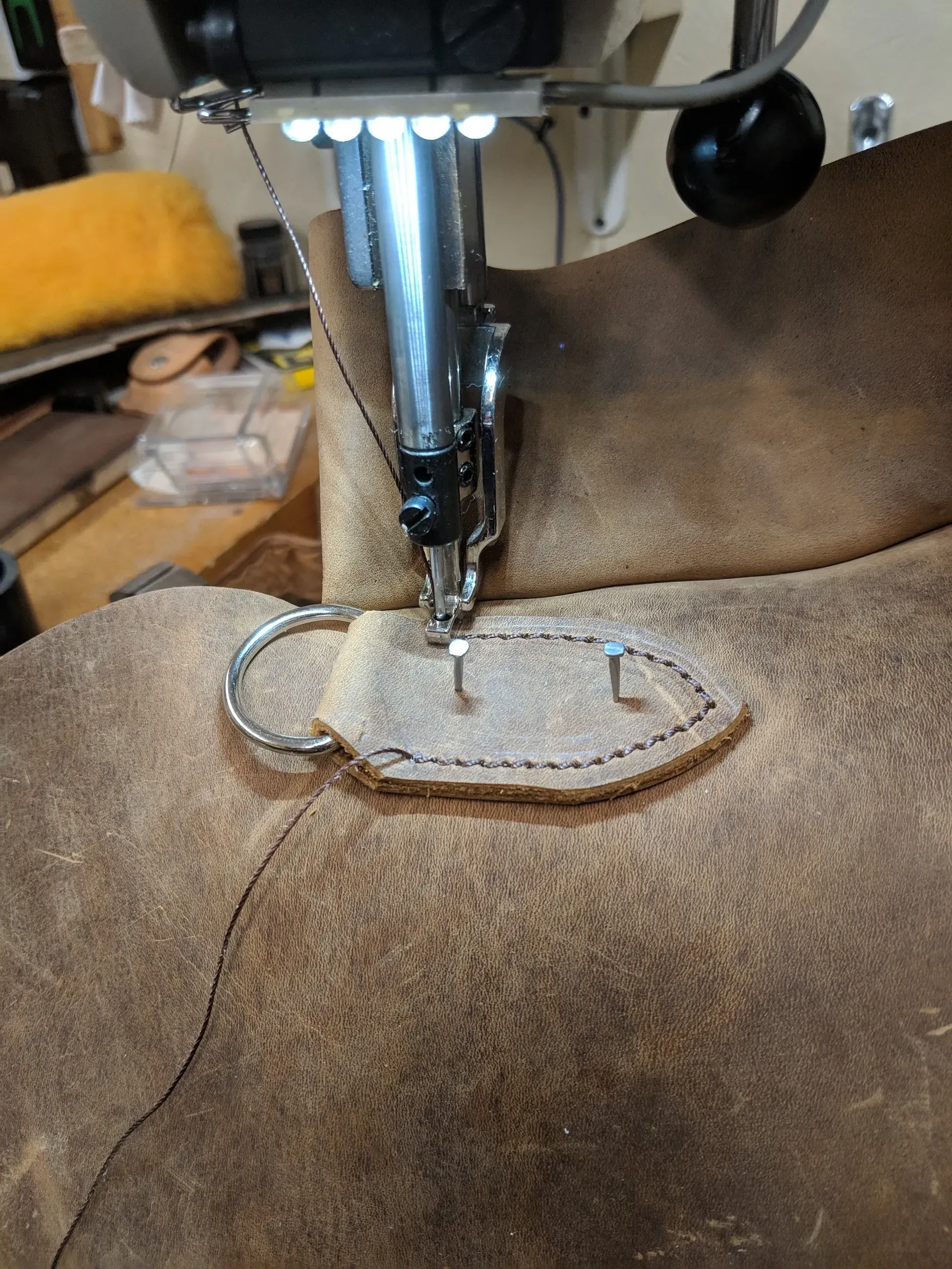 Sewing machine stitching a brown felt piece with a metal ring attached