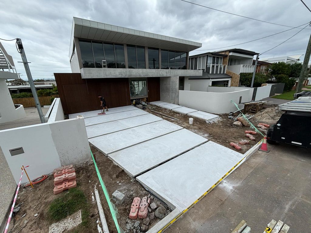 Modern home under construction with concrete driveway and cloudy sky.