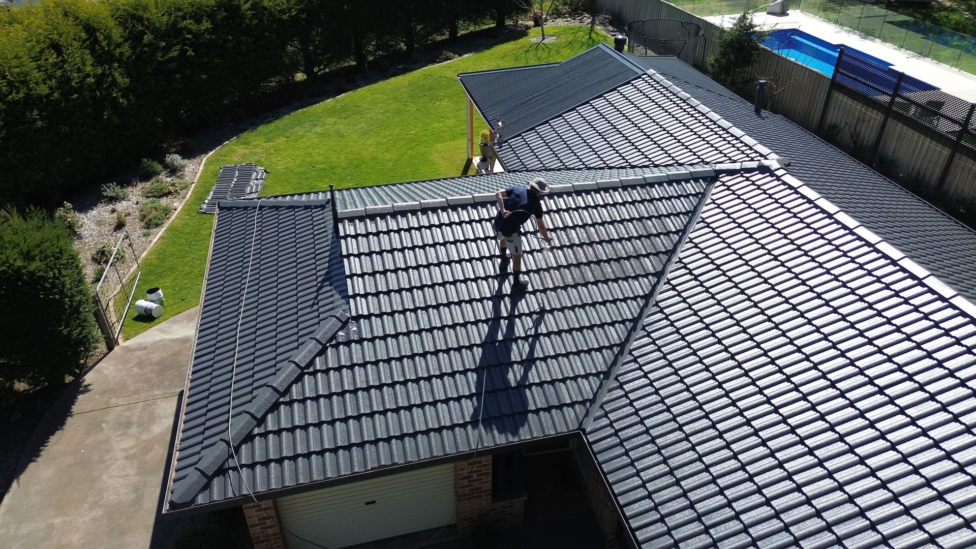 Person on a dark gray tiled roof, sunny day, residential property.