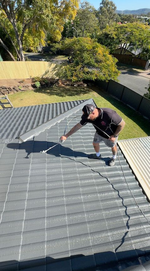 Man on a roof examines a crack. Gray tiles, green trees, and blue sky in the background.