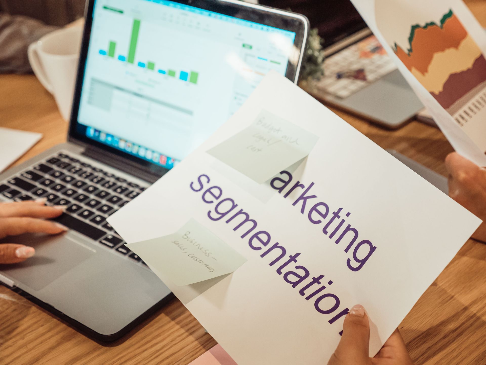 Person reviewing marketing segmentation notes beside a laptop with charts on screen