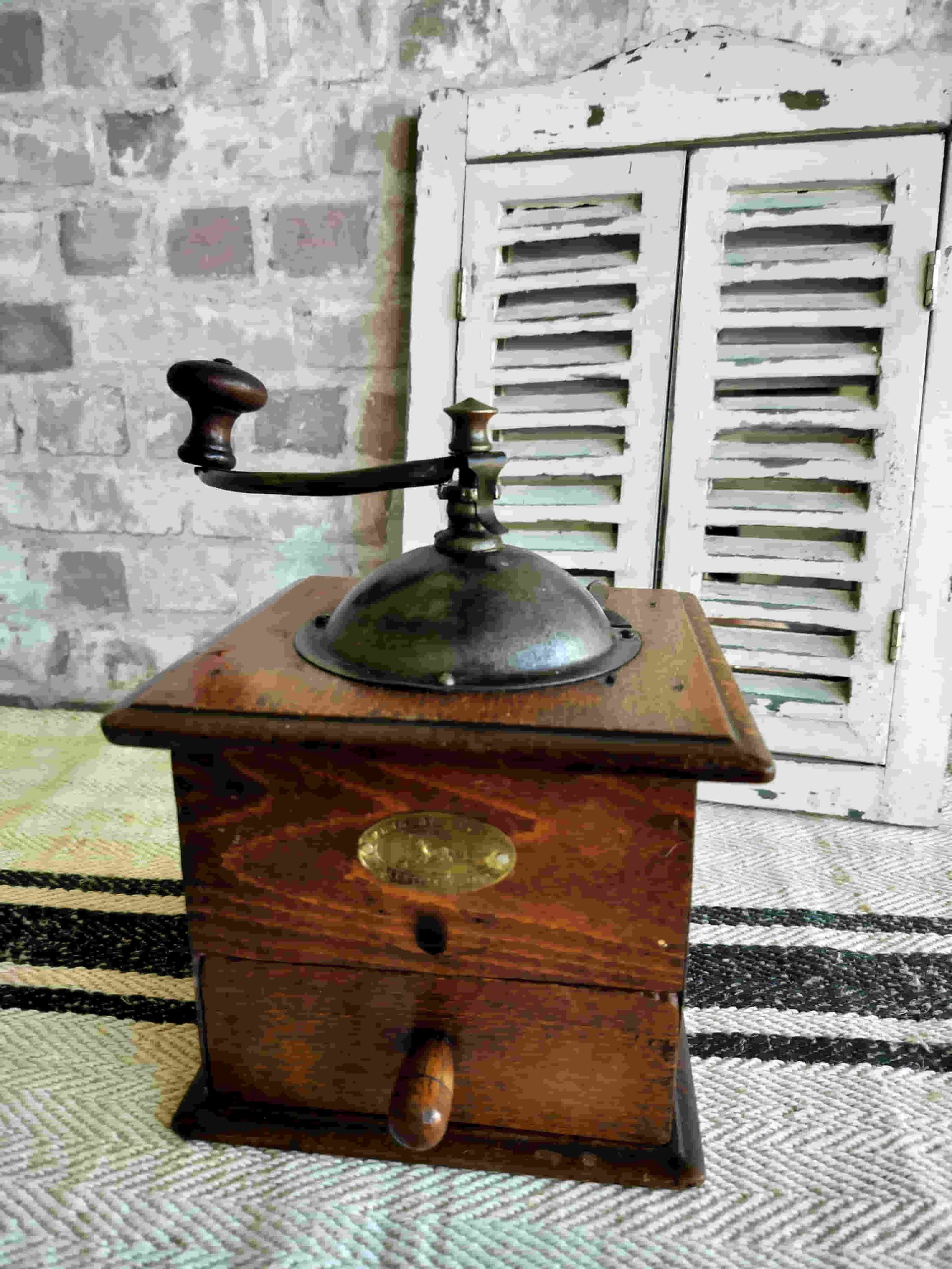 A wooden coffee grinder is sitting on a rug in front of a window with shutters