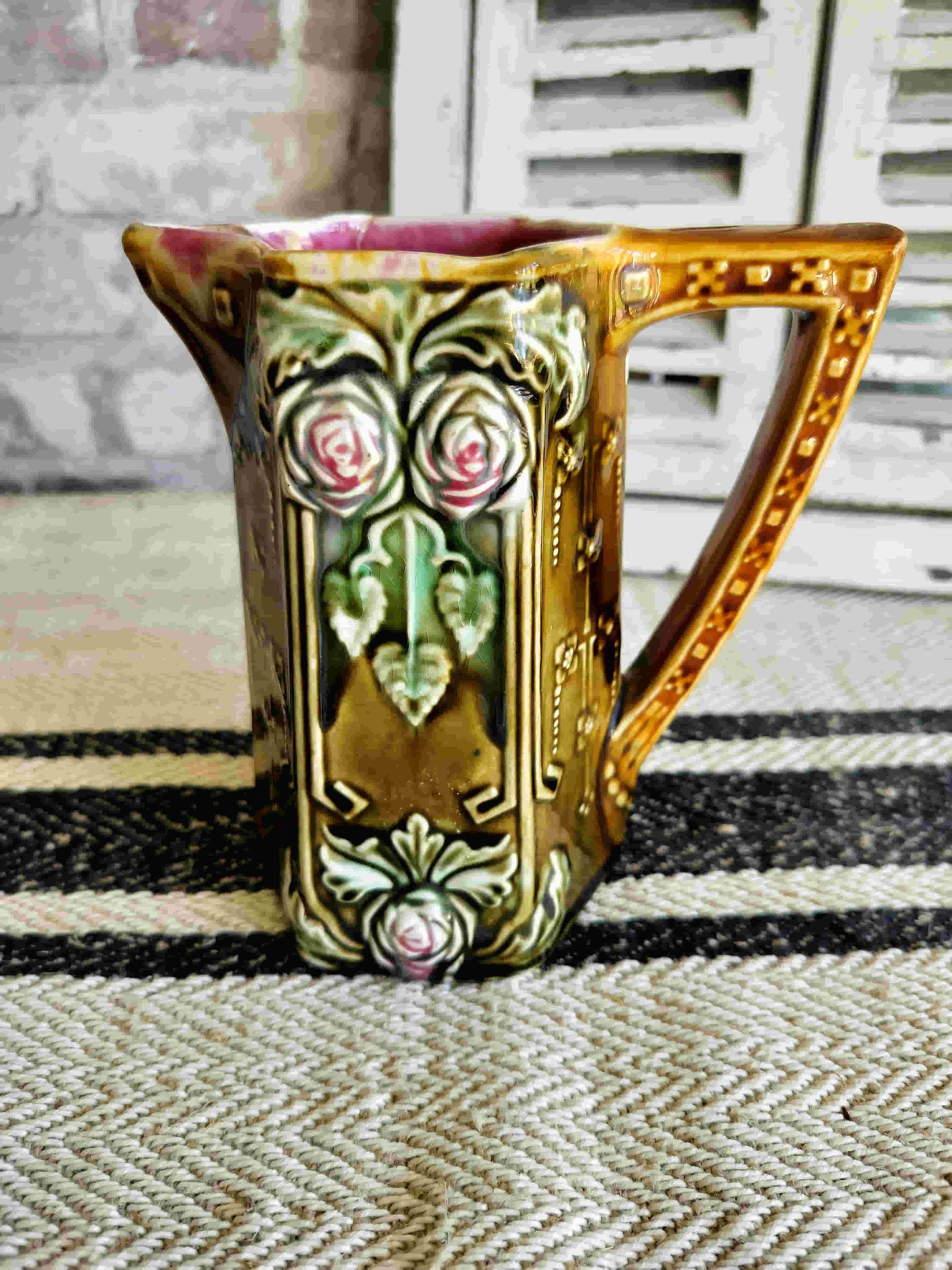A pitcher with roses on it is sitting on a rug.
