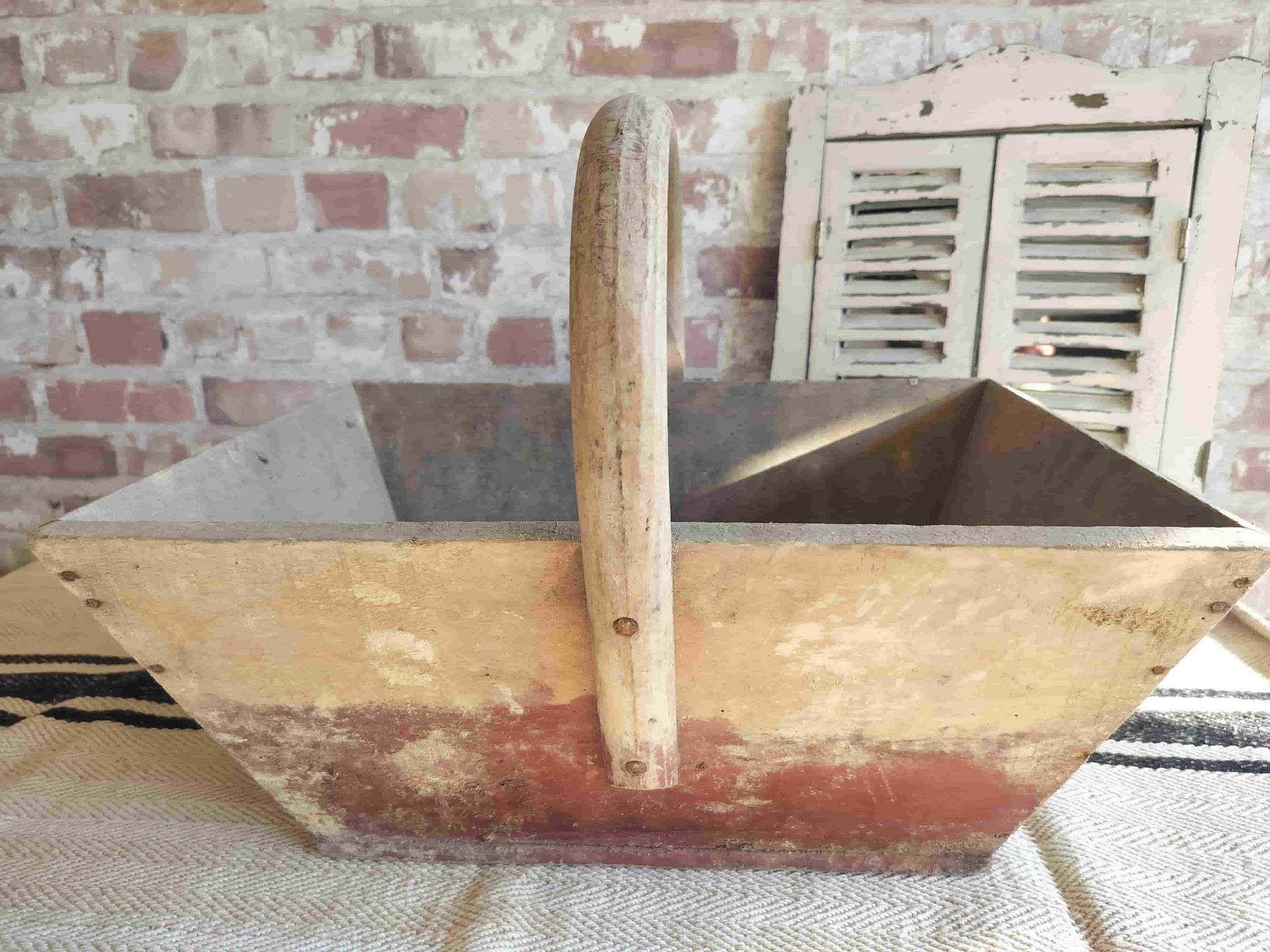 A wooden basket with a wooden handle is sitting in front of a brick wall