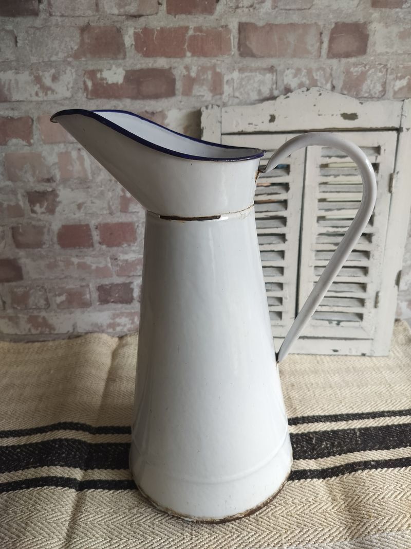 A white pitcher is sitting on a table in front of a brick wall.
