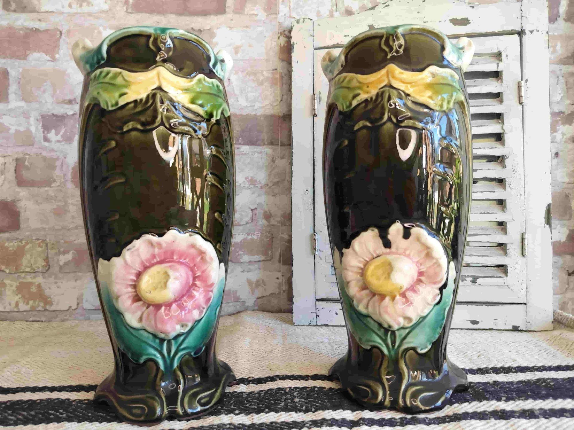 Two vases with flowers on them are sitting on a rug in front of a brick wall.