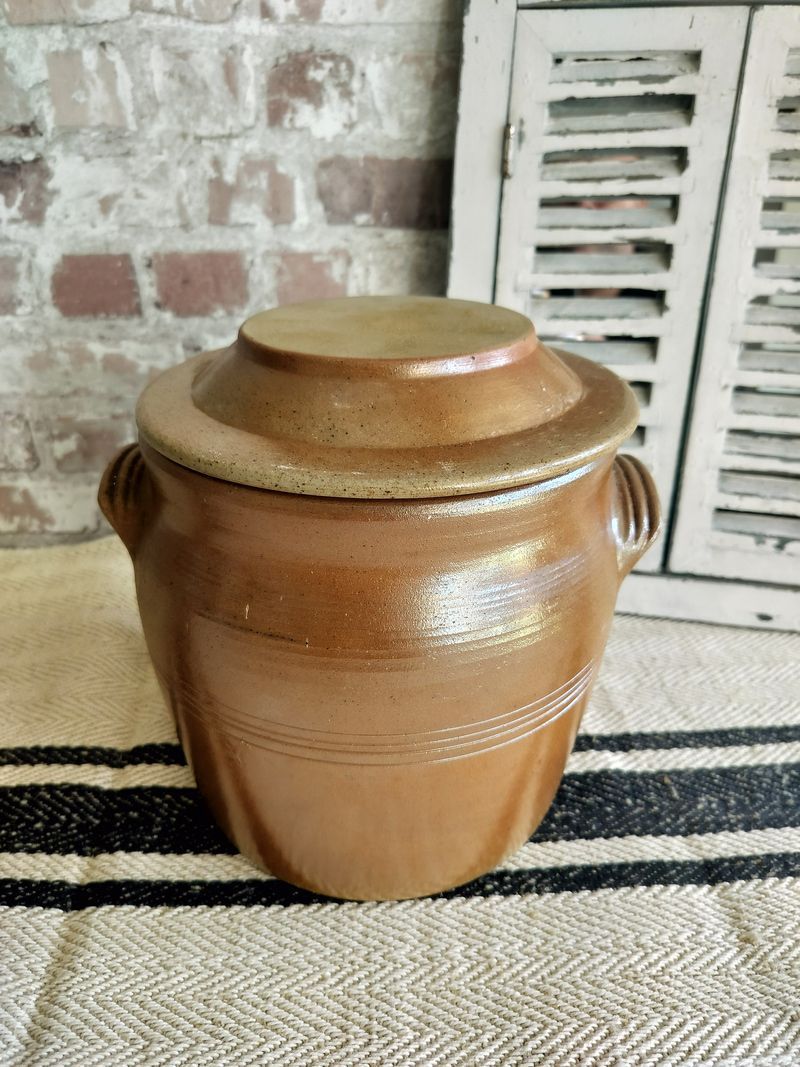 A brown pottery jar with a lid is sitting on a striped rug.