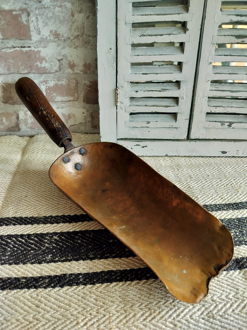 A copper shovel with a wooden handle is sitting on a rug.
