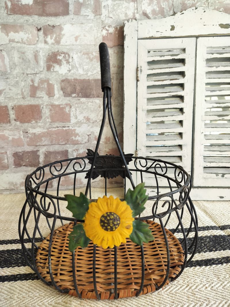 A wire basket with a sunflower in it is sitting on a rug in front of a brick wall.