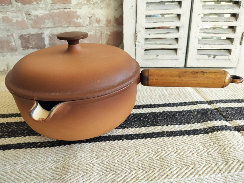 A brown pot with a wooden handle is sitting on a rug