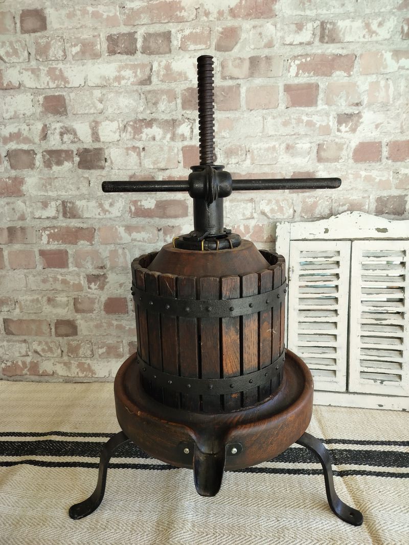 A wooden wine press is sitting on a rug in front of a brick wall.
