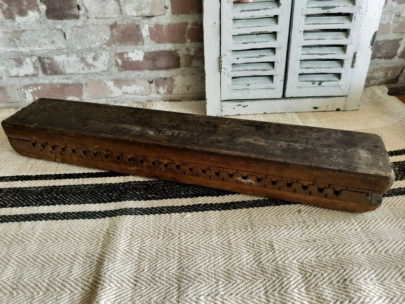 A long wooden box is sitting on a rug in front of a brick wall.