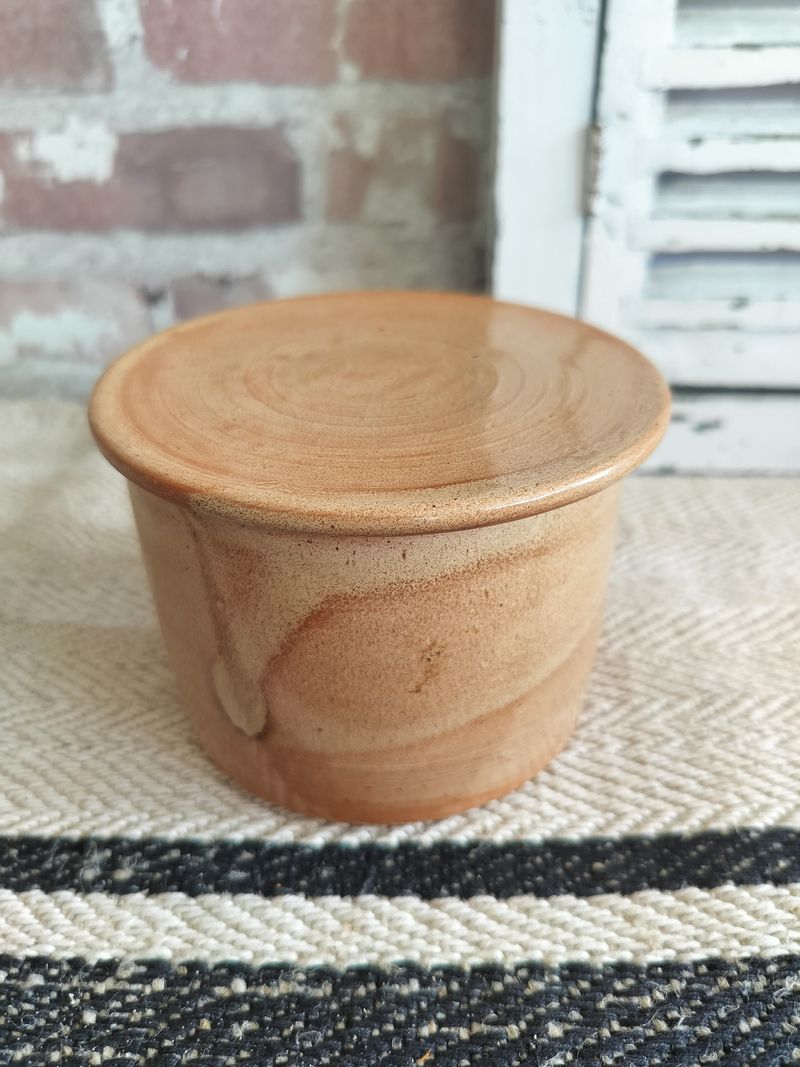 A small brown bowl is sitting on a rug next to a brick wall.