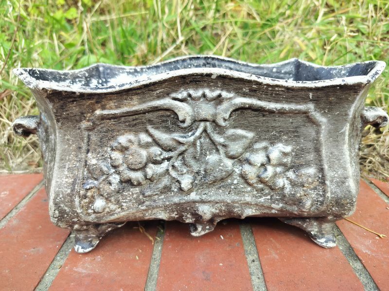 A metal planter with flowers on it is sitting on a brick floor