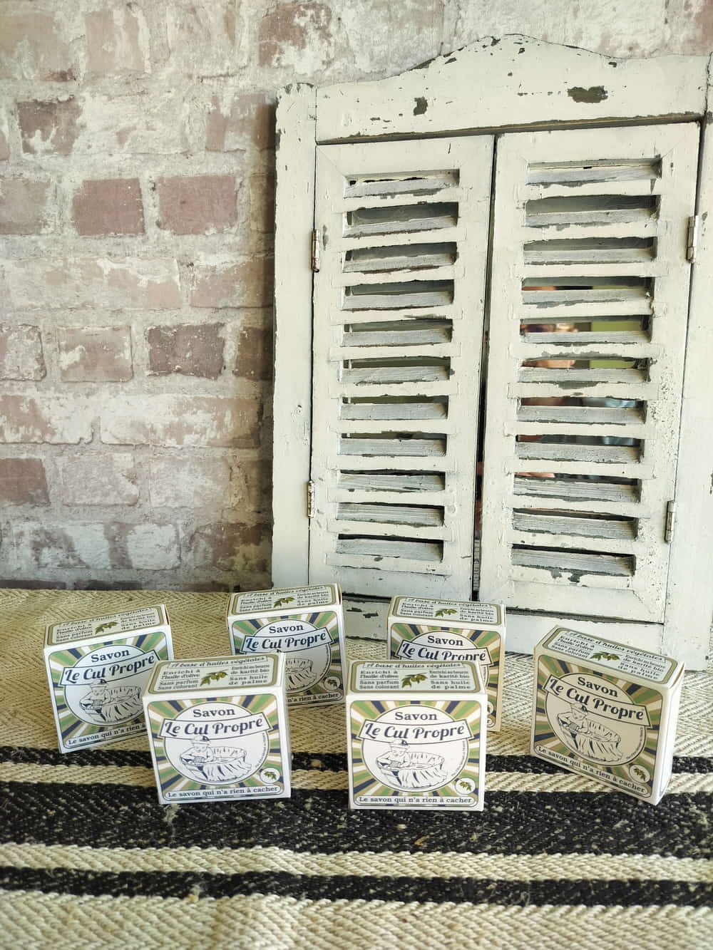 A group of boxes of soap are sitting on a rug in front of a window with shutters.