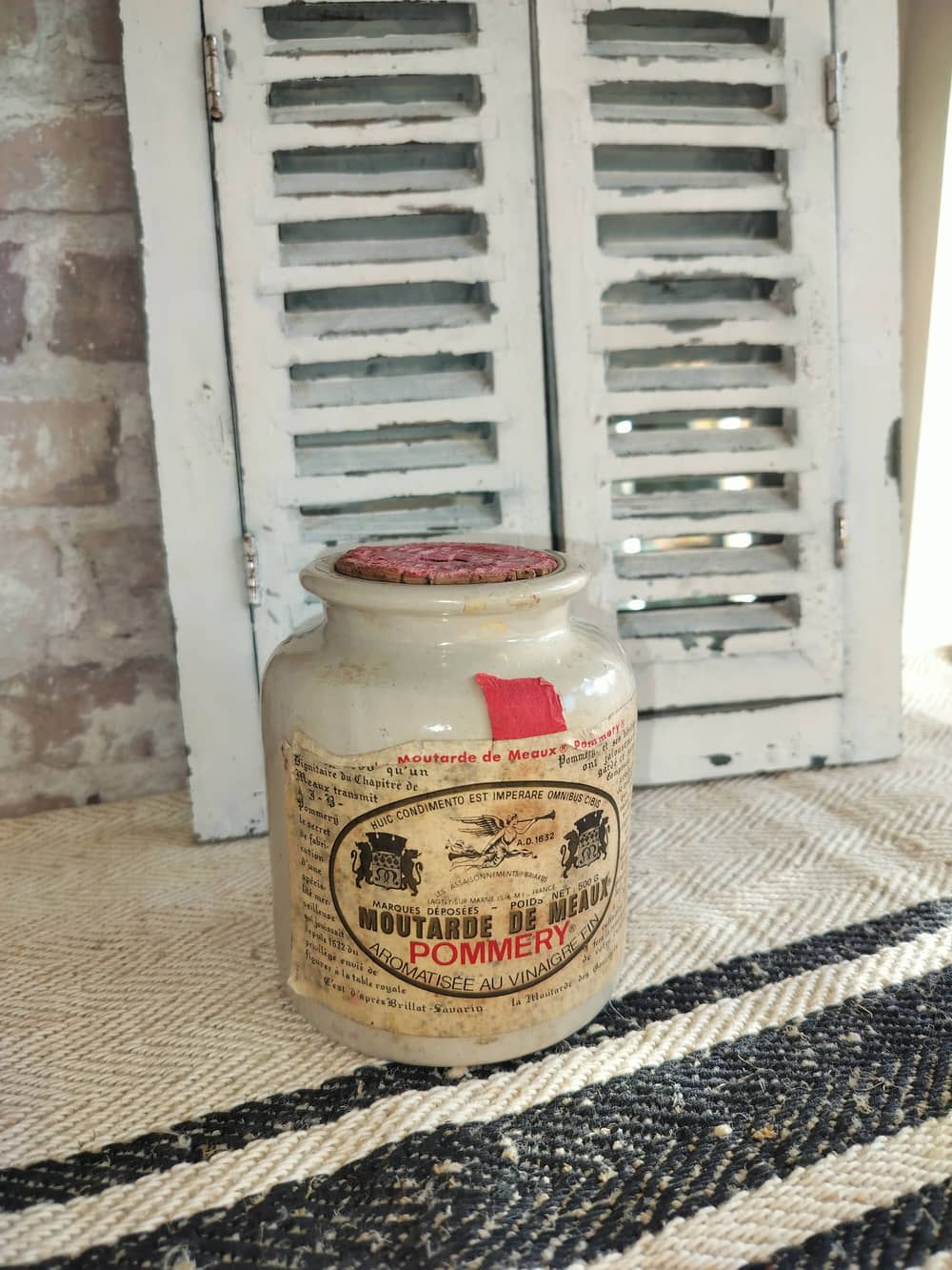 A small jar is sitting on a rug in front of a window.