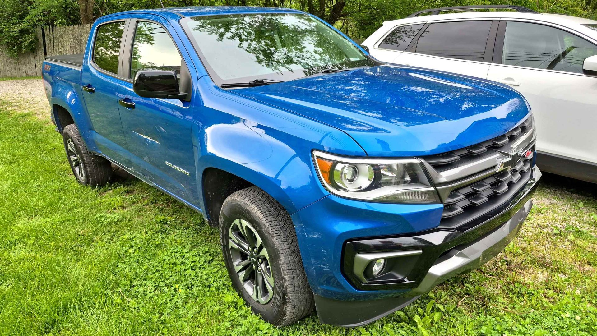 Blue Chevrolet Colorado truck parked on grass next to a white SUV.