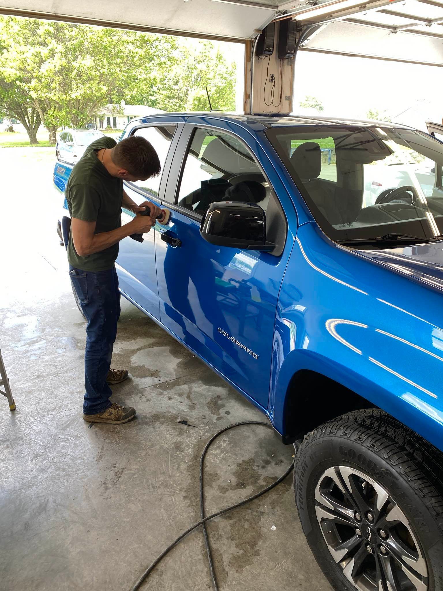 Man working on the door handle of a blue truck inside a garage.