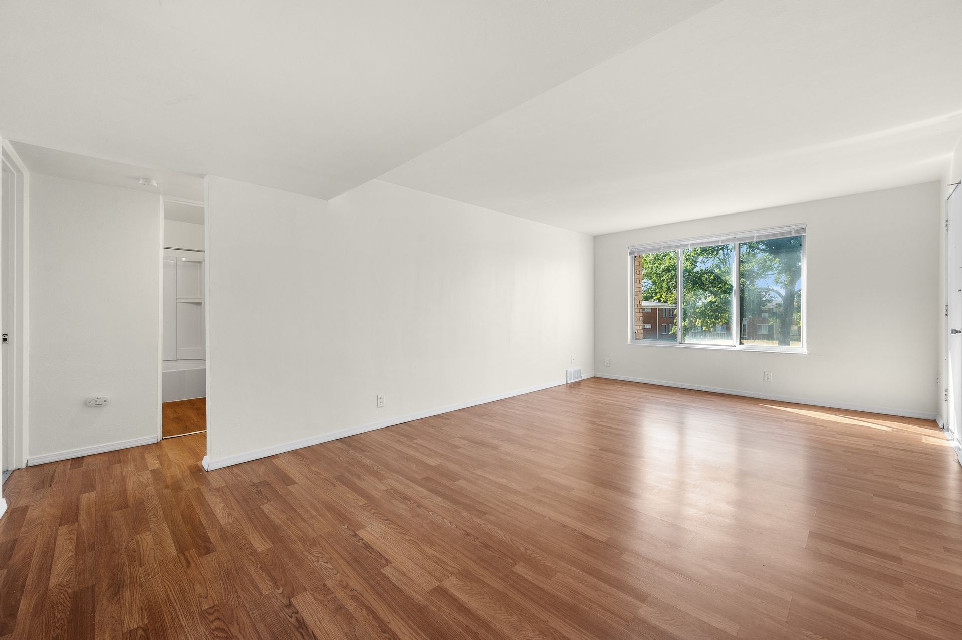 An empty living room with hardwood floors and white walls.