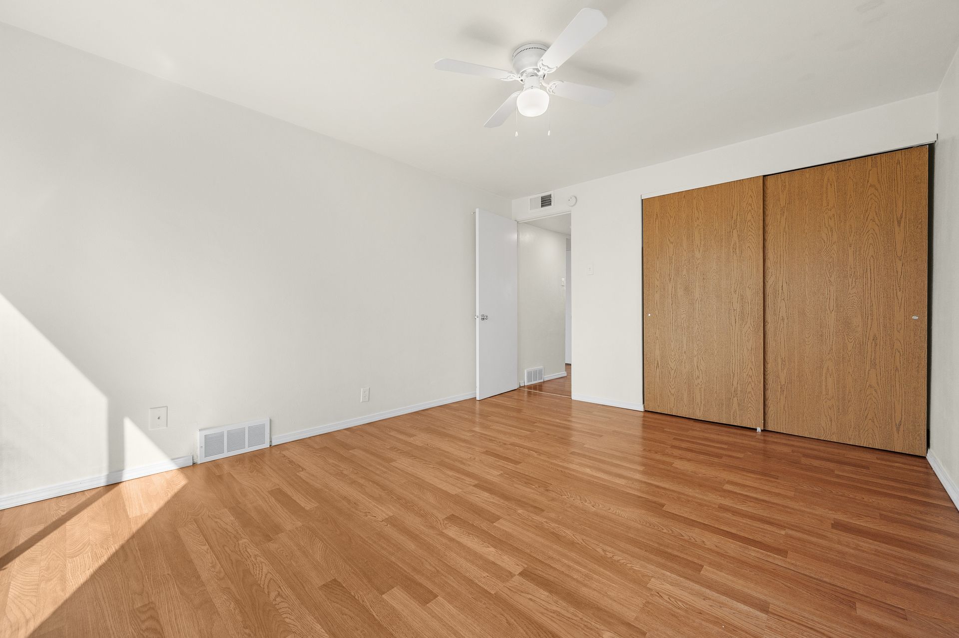 An empty bedroom with hardwood floors and a ceiling fan.