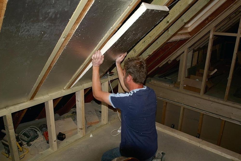 Skilled contractor fitting insulation into the roof of a constructed home, ensuring energy efficiency and temperature regulation.