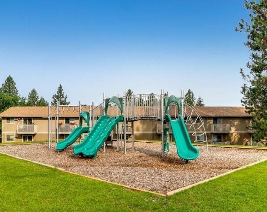 a playground with green slides and swings in front of a building .