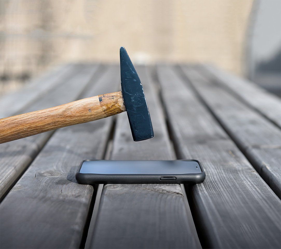 A hammer is hitting a cell phone on a wooden table.