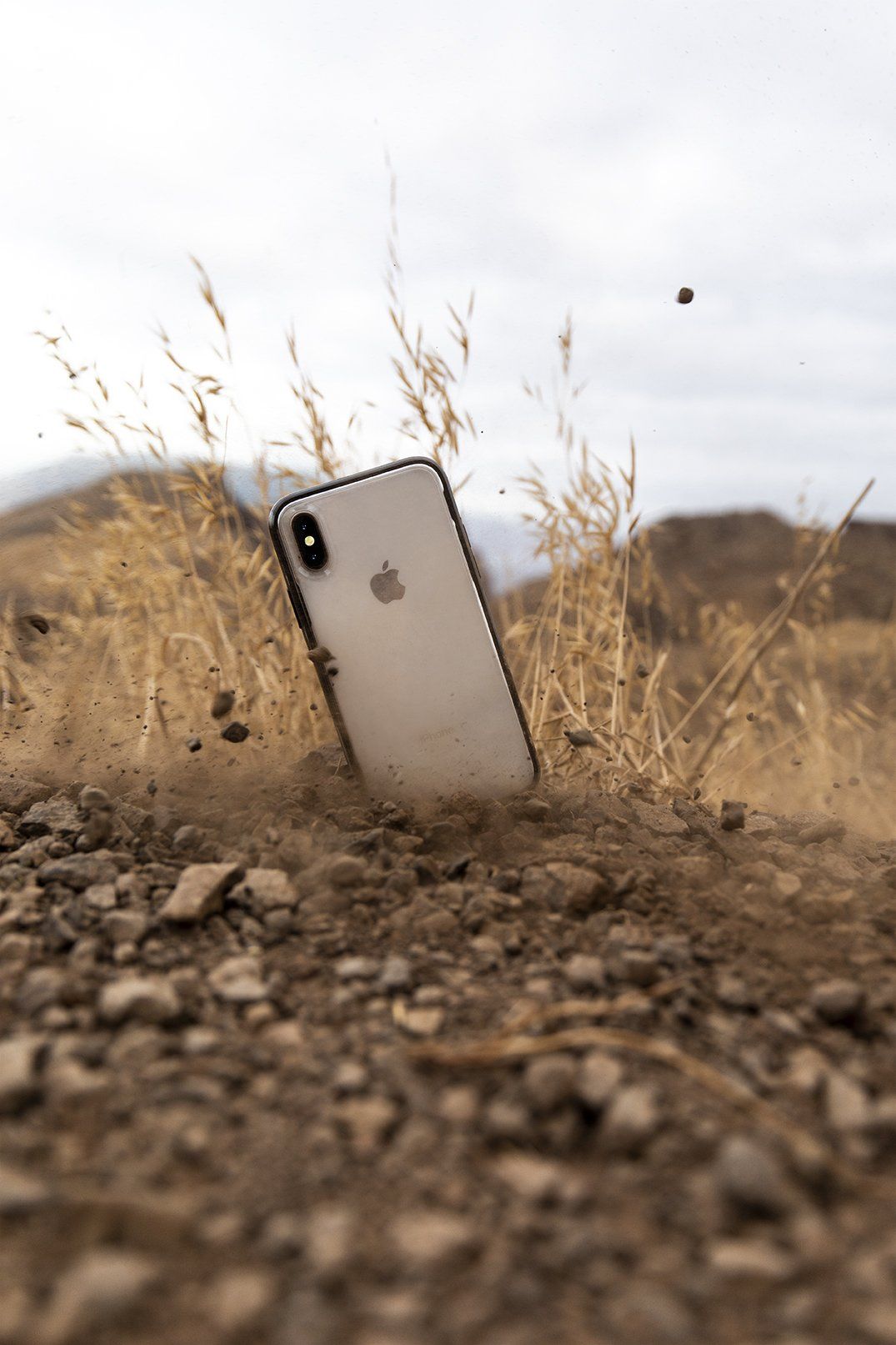 An apple iphone is laying on the ground in the dirt.