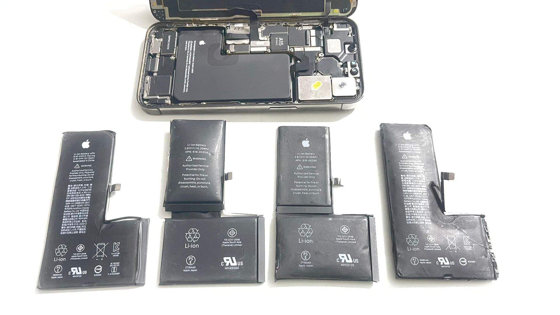 A bunch of iPhone batteries are sitting next to each with an open iPhone above them.