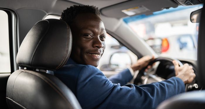 A man in a suit is driving a car and smiling.