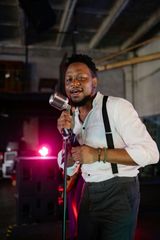 A man in a white shirt and suspenders is singing into a microphone.