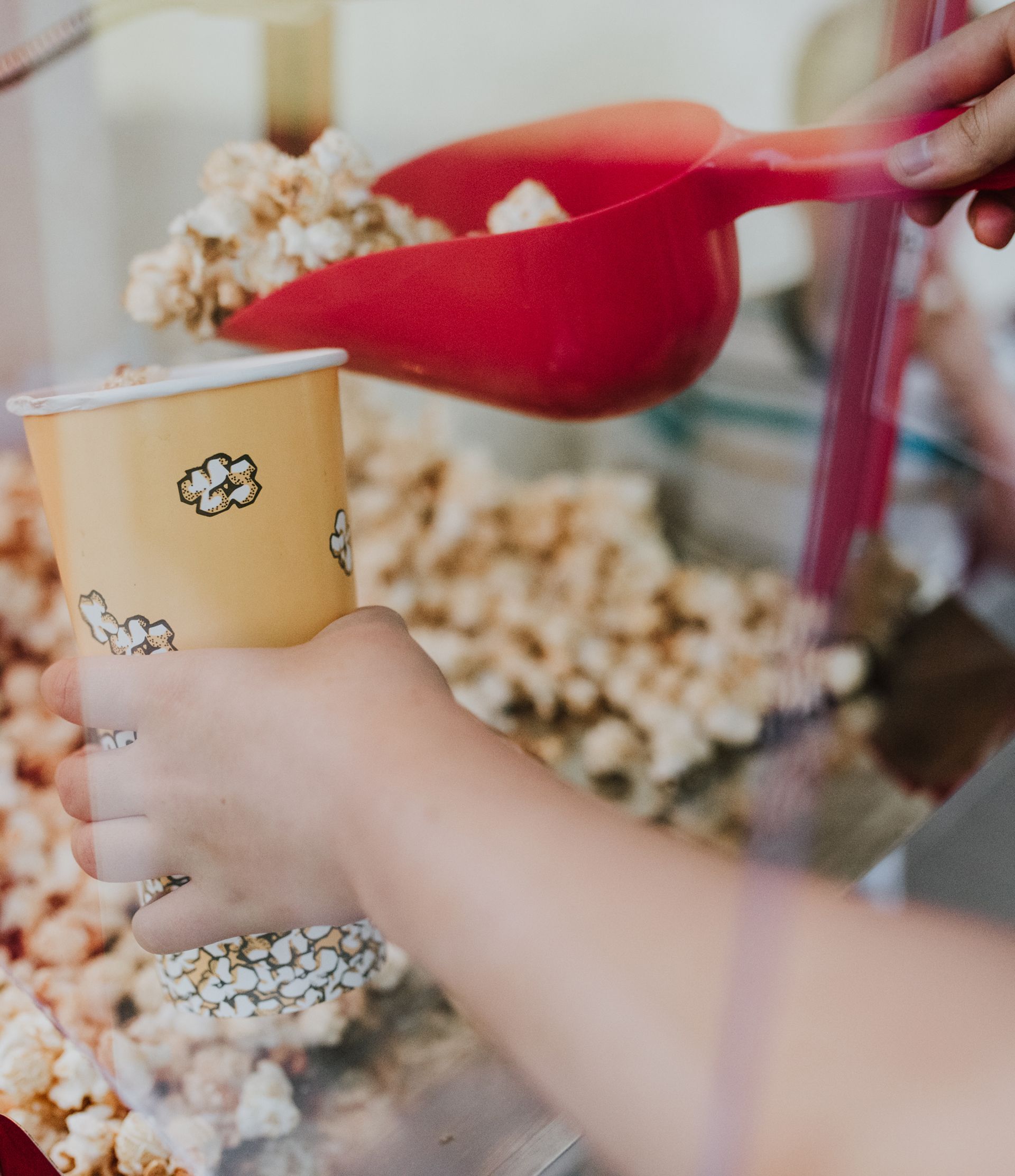 A person is pouring popcorn into a paper cup. A person is pouring popcorn into a paper cup.