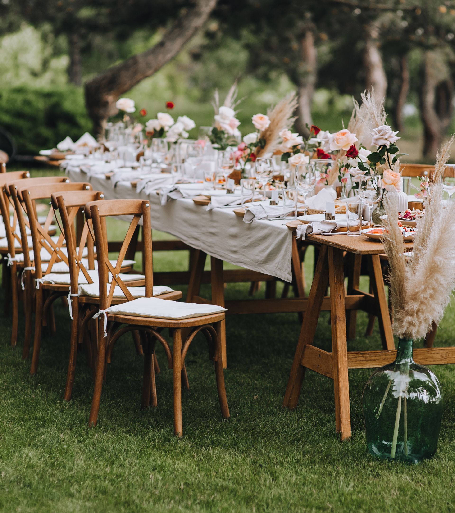 A long table with chairs and flowers on it is sitting on top of a lush green field. A long table with chairs and flowers on it is sitting on top of a lush green field.
