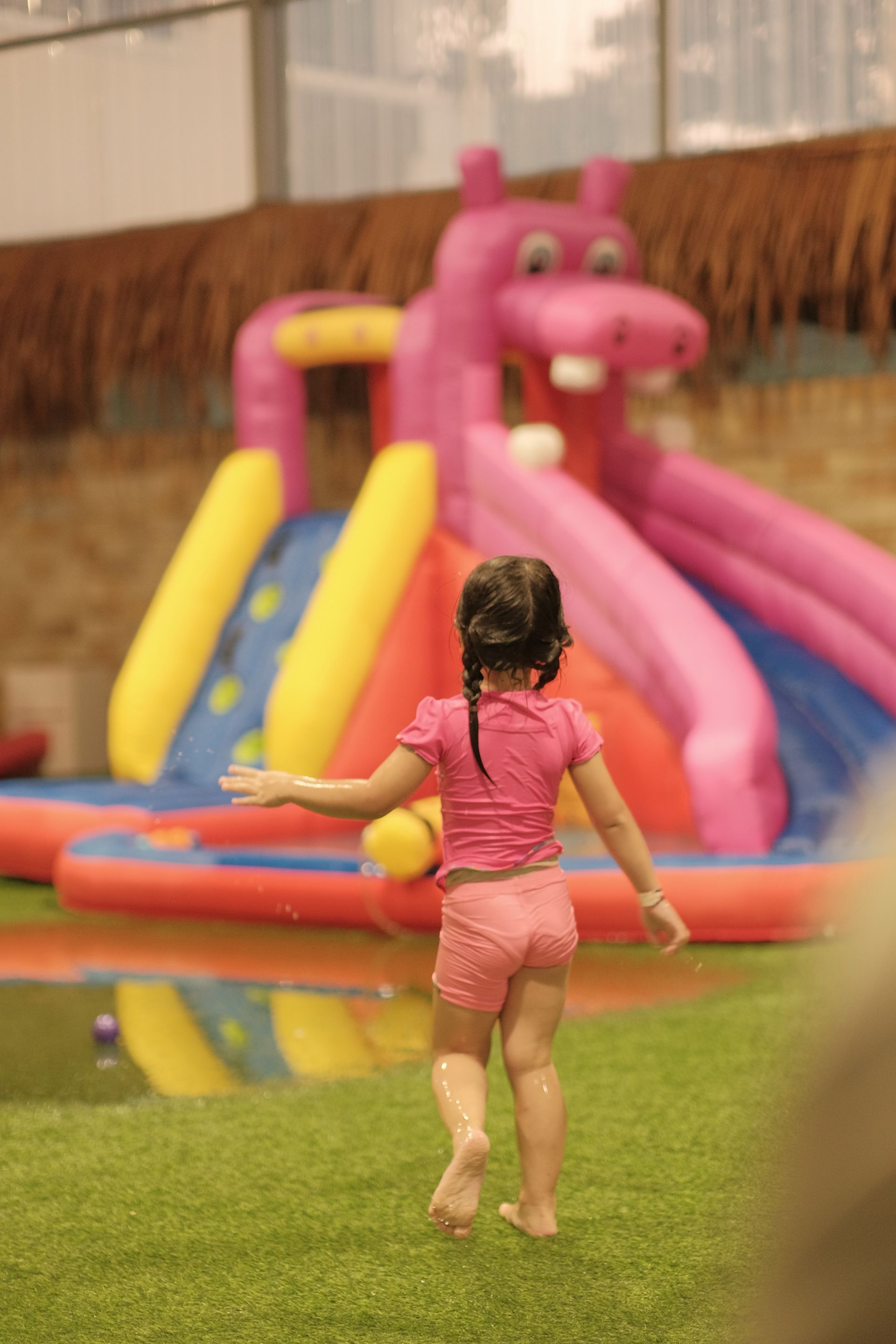 A little girl is running towards a pink inflatable hippo water slide. A little girl is running towards a pink inflatable hippo water slide.