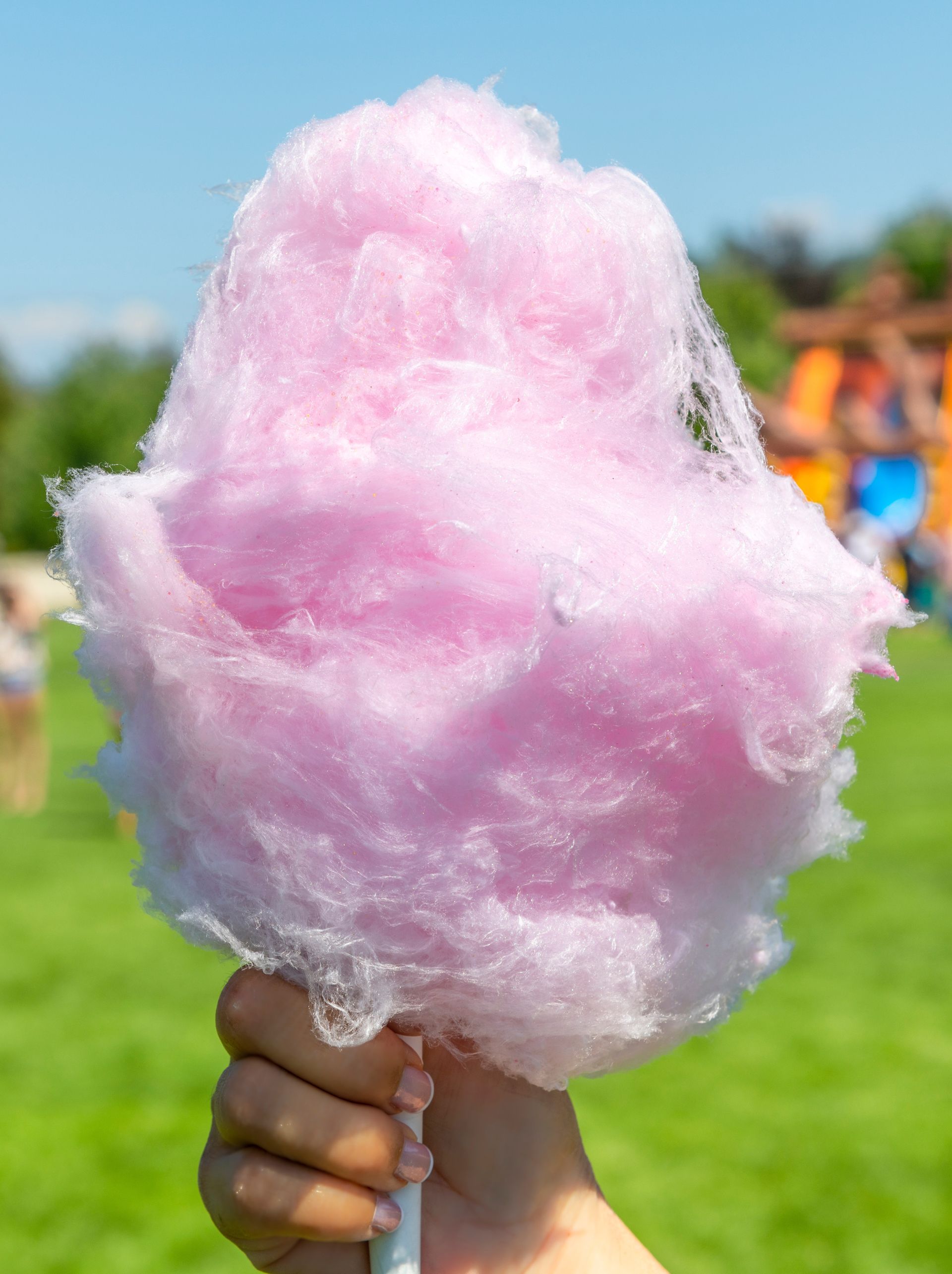 A person is holding a pink cotton candy on a stick. A person is holding a pink cotton candy on a stick.