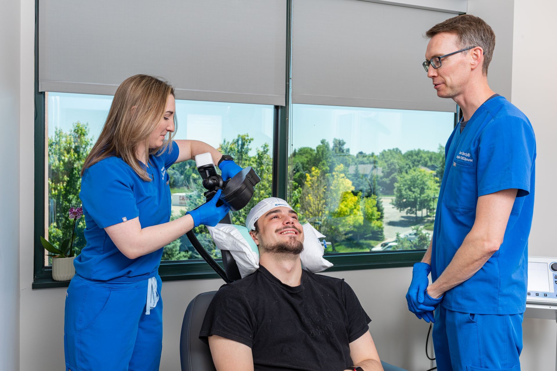 A man receives a medical procedure with the help of two medical professionals in a clinic setting.