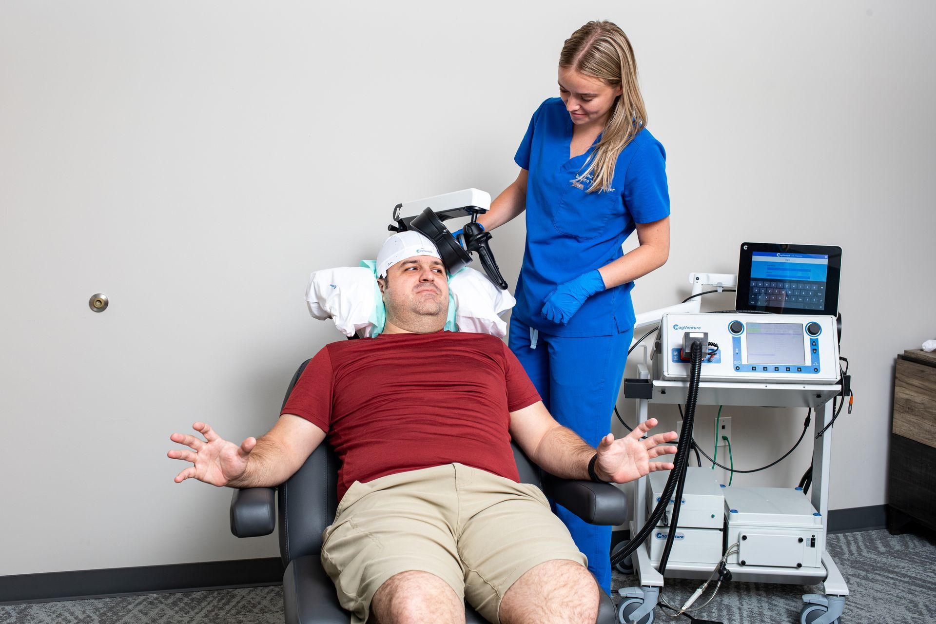 A patient in a treatment chair receives TMS therapy as a practitioner adjusts the device near their head.
