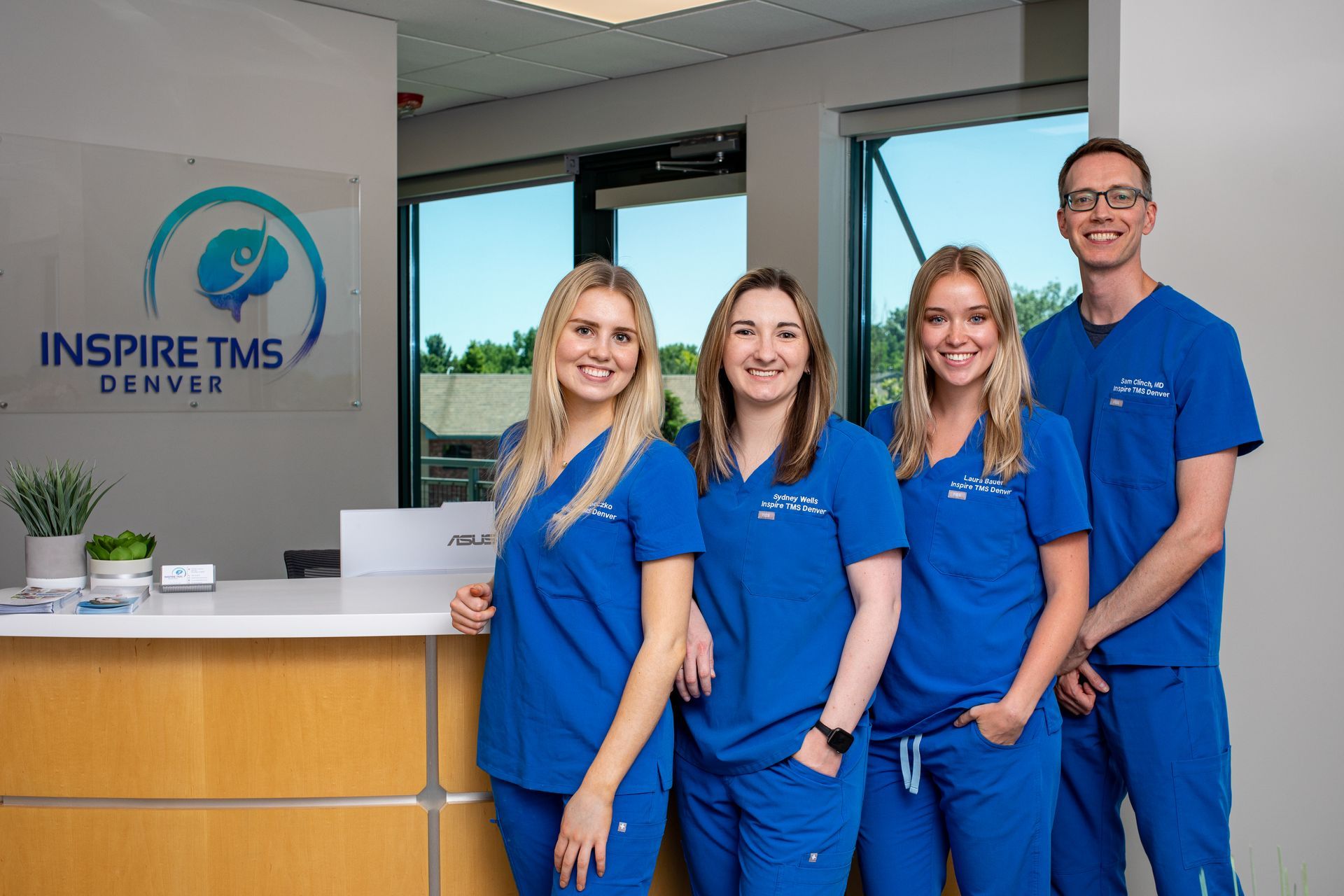 Four people in blue scrubs standing at an Inspire TMS Denver reception desk