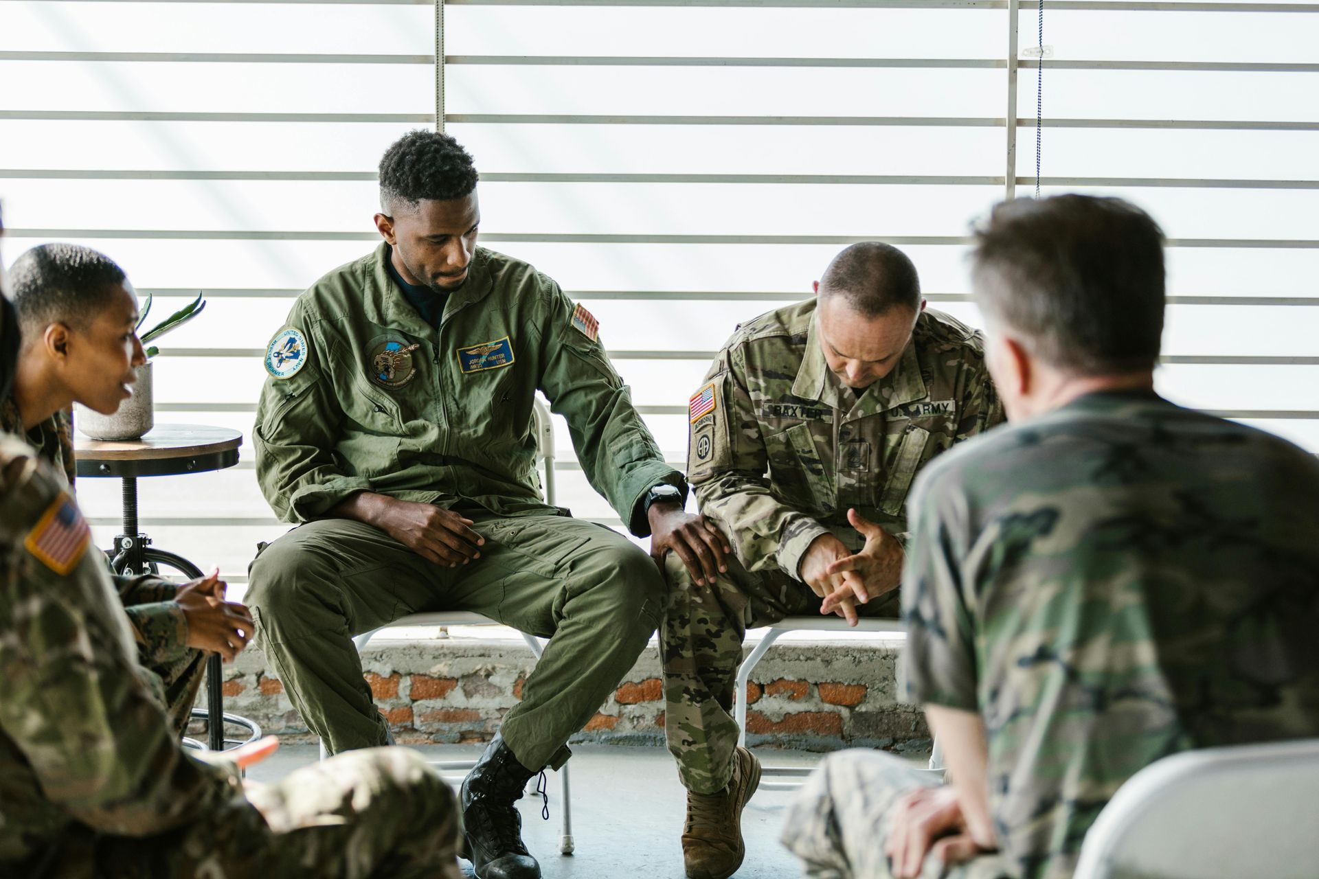 Soldiers in uniform seated in a circle; one person comforts another, all in a support group setting.