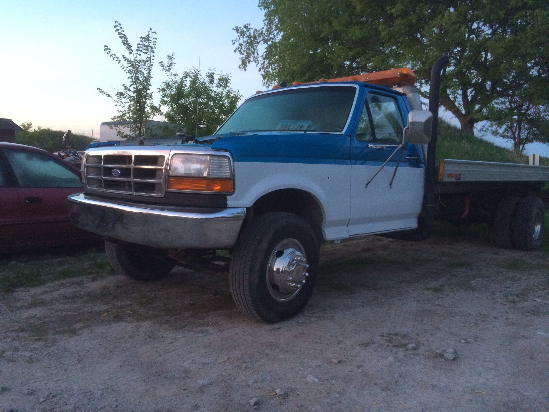 Blue and white Ford flatbed truck parked on a dirt lot.