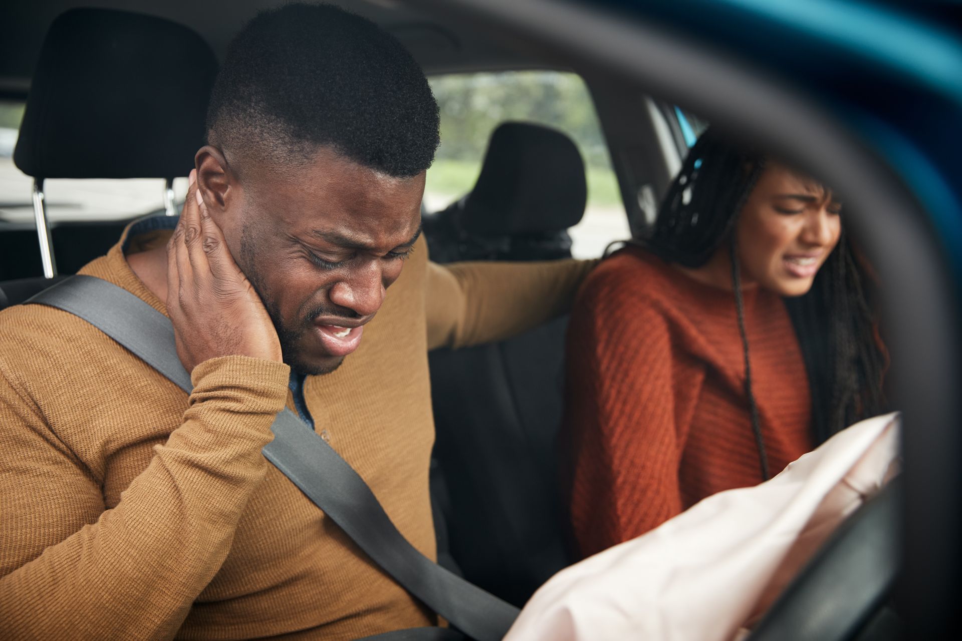 Two people in crashed car with airbags deployed, one holding neck after impact. Two people in crashed car with airbags deployed, one holding neck after impact.