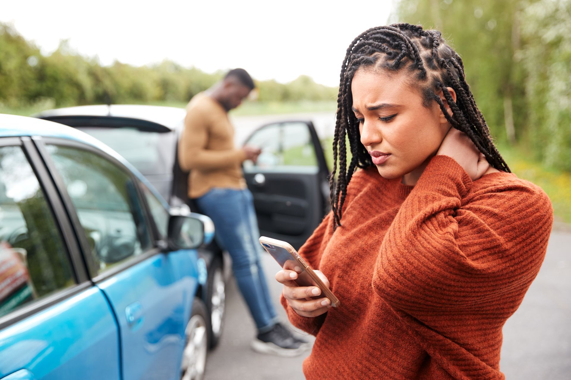 Person holding phone and touching neck beside damaged cars after a roadside collision. Person holding phone and touching neck beside damaged cars after a roadside collision.